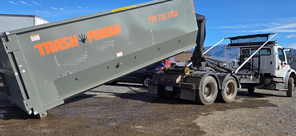 A Trash Panda roll-off truck lowering a branded dumpster onto the ground in Carson City, NV.
