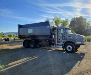A roll-off truck with a dumpster featuring the company logo, parked at a job site for Premier Recycling and Disposal in Waukesha, WI.
