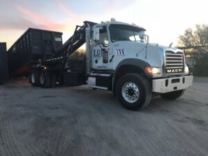 A white LDI roll-off truck with a large black dumpster on its back, parked at sunset for Liberty Disposal, Inc. in Tucson, AZ.