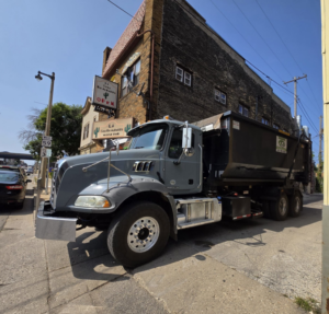 A roll-off truck with a dumpster parked on a city street in a commercial area for Premier Recycling and Disposal in Waukesha, WI.