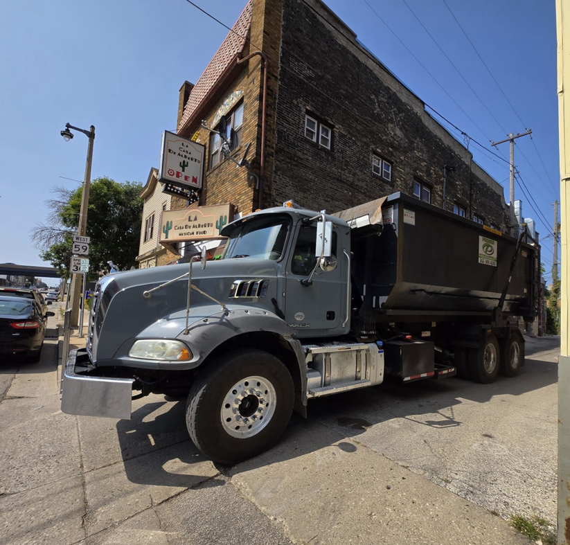 A roll-off truck with a dumpster parked on a city street in a commercial area for Premier Recycling and Disposal in Waukesha, WI.