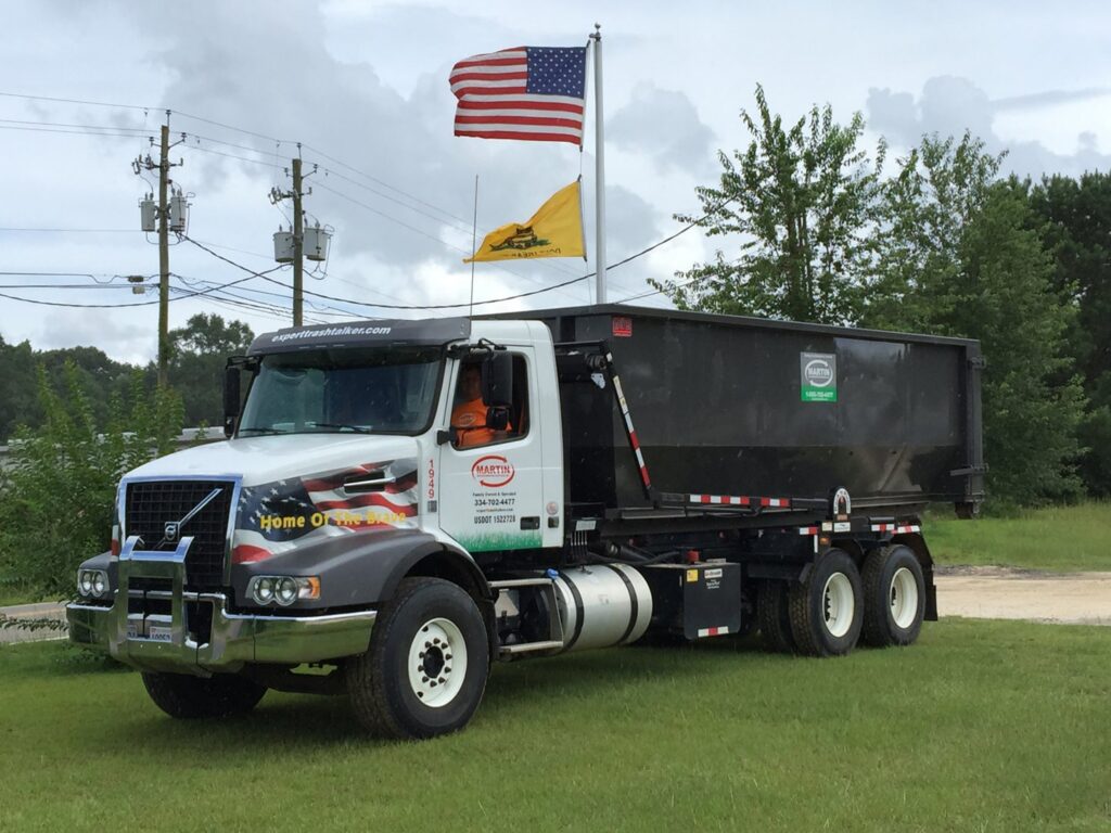 A Martin Environmental roll-off truck with a large dumpster parked under American flags in Dothan, AL.