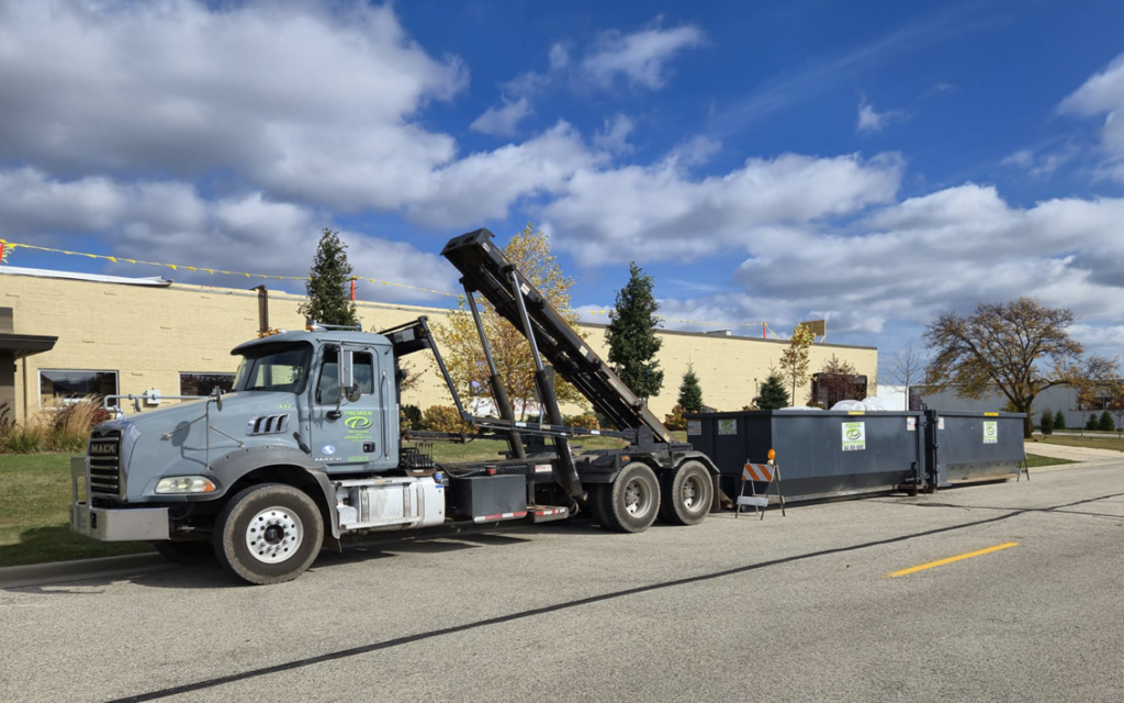 A roll-off truck with a dumpster attached, parked on a street for Premier Recycling and Disposal in Waukesha, WI.