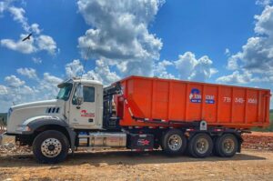 A Tenn-Scrap roll-off truck transporting an orange dumpster for junk removal services in Jackson, TN.