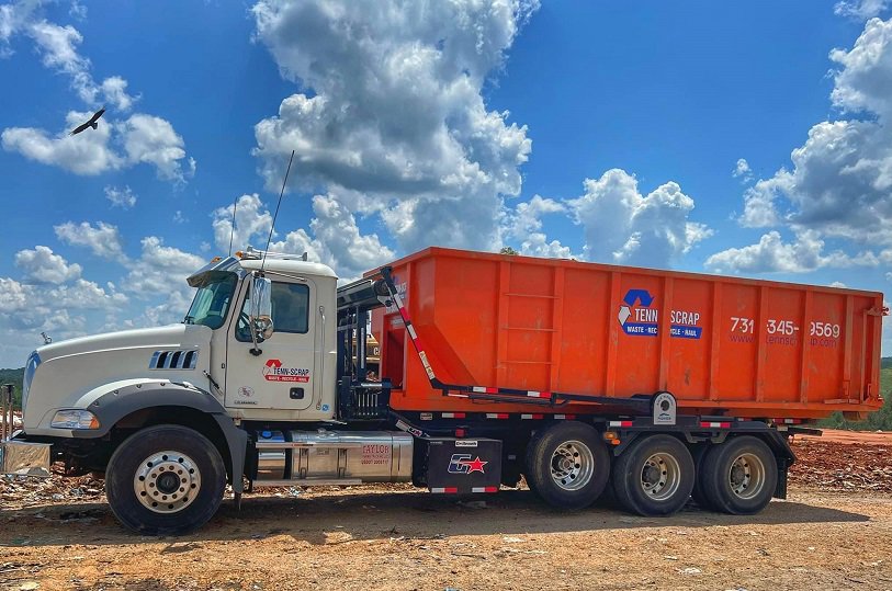 A Tenn-Scrap roll-off truck transporting an orange dumpster for junk removal services in Jackson, TN.