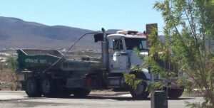 A white roll-off truck with a green dumpster, branded A Track-Out Solution, parked in Las Vegas, NV.
