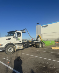 A Top Line Dumpsters LLC roll-off truck with a green dumpster at an Amazon facility in Hammond, LA.