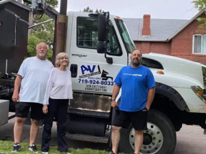 A white roll-off truck with the Arkansas Valley Roll-Off logo and three team members in Salida, CO.