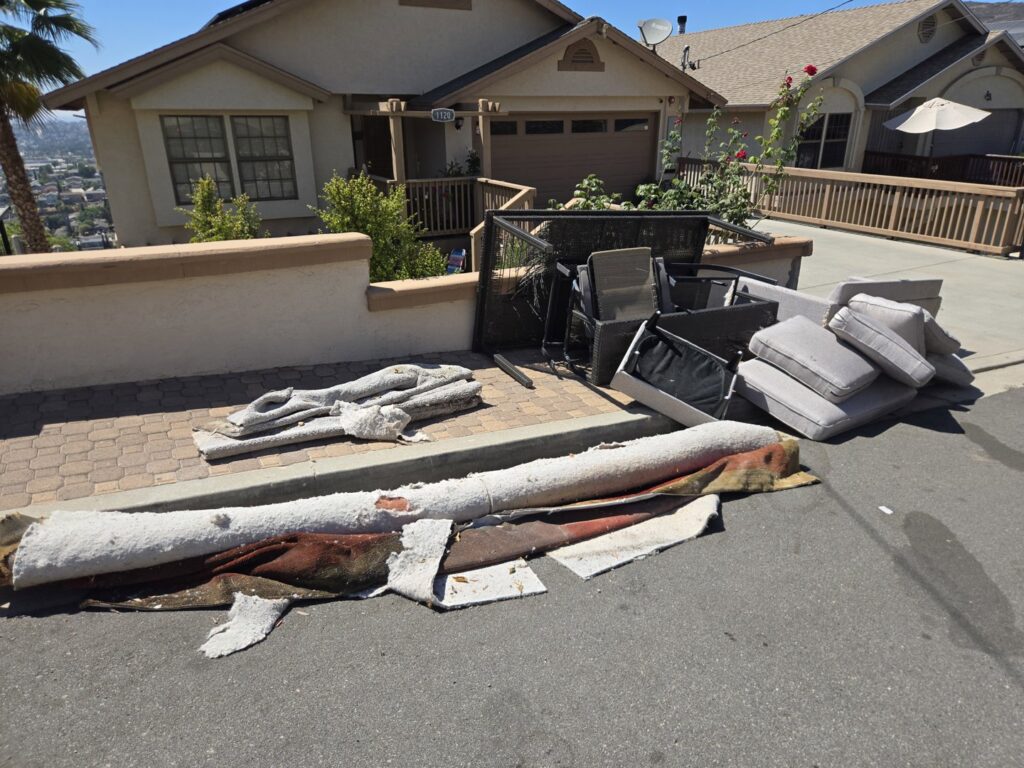 Rolled carpets, outdoor furniture cushions, and other junk piled on a driveway for removal by Titan Junk Co. in San Diego, CA
