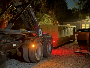 A roll-off truck deploying a large yellow dumpster for junk removal services by Tecumseh Rolloff Services in Moore, OK.