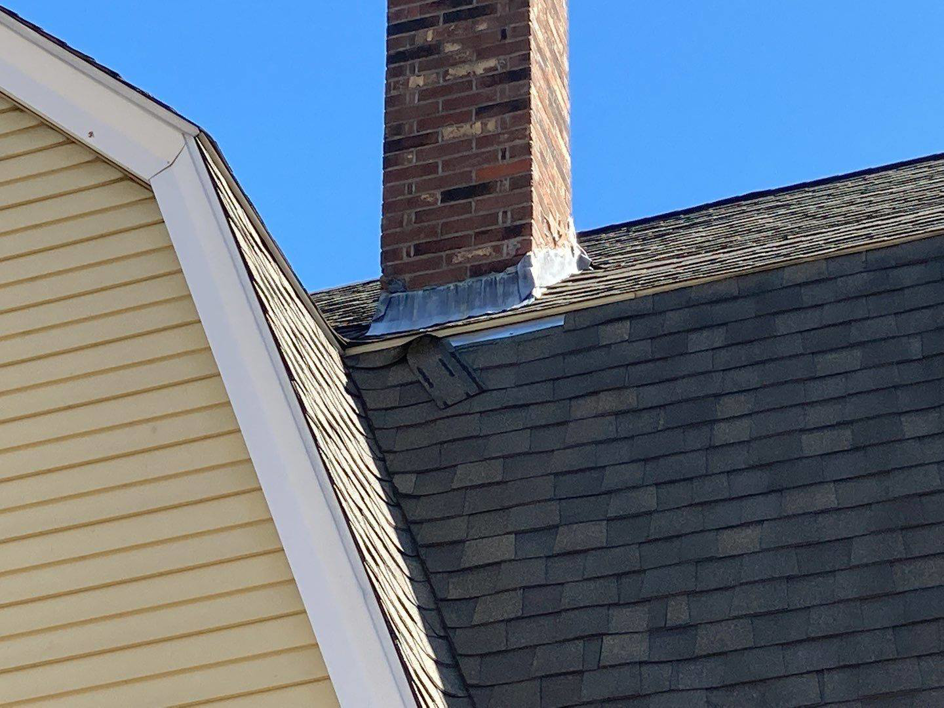 A roof with a brick chimney showing potential flashing damage and displaced shingles, requiring repair by The Roof Guy in Fort Lauderdale, FL.