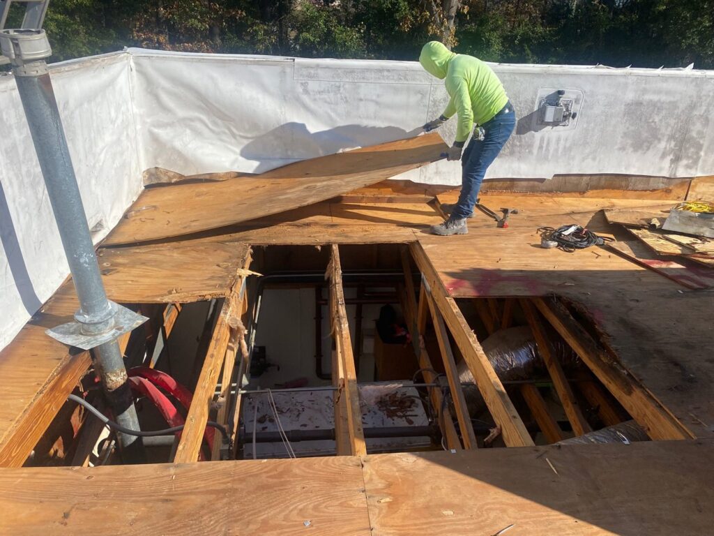 A worker removing old roof decking, preparing for a full roof replacement by Roofing Experts Care in Charlotte, NC.