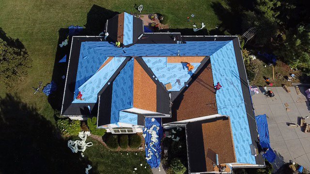 An aerial view of a residential roof installation in progress with blue underlayment, by First Contracting Group in Rockford, IL.