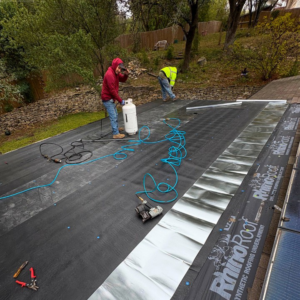 Workers installing synthetic roofing underlayment on a residential roof for Vargas Paint and Texture in San Antonio, TX.