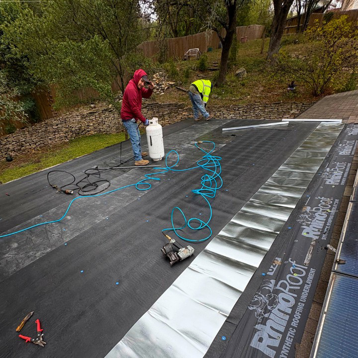 Workers installing synthetic roofing underlayment on a residential roof for Vargas Paint and Texture in San Antonio, TX.