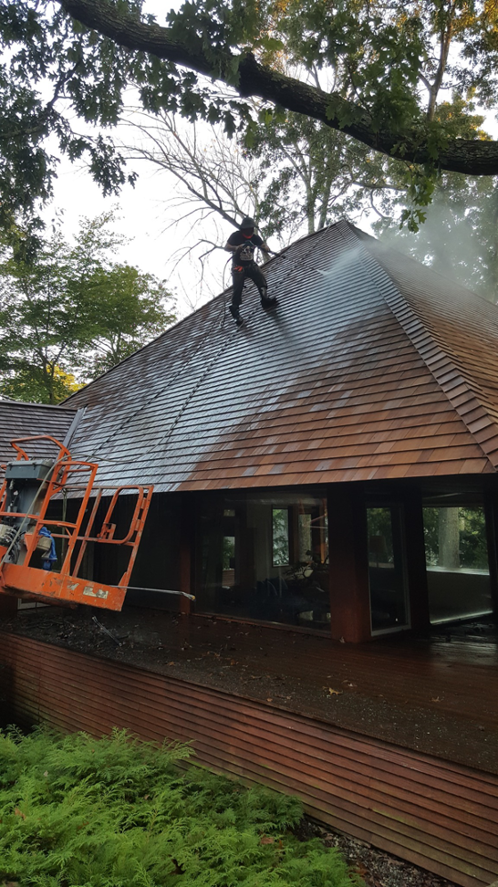 A professional performing roof power washing service on a residential home at Superior Power Wash in Danbury, CT.