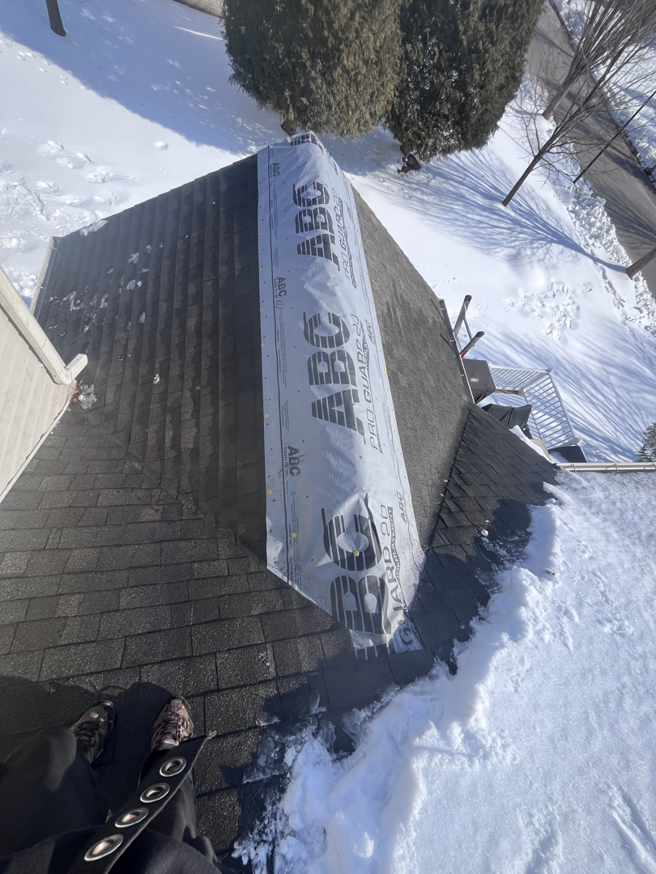 An aerial view of a roof with snow, showing a section covered with a protective membrane during repair or installation by Crown Remodeling in Owings Mills, MD.