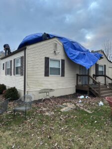 A worker on a roof covered with a blue tarp, performing roof repair for SHIFT Roofing & Exteriors in Gahanna, OH