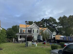 Workers on a roof with a crane delivering materials for a roof replacement by Coastal Roofing Solutions LLC in Charleston, SC.