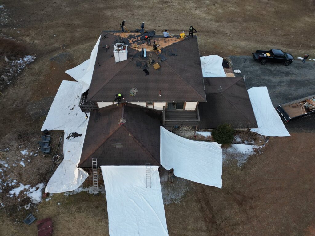 Aerial view of a house undergoing roof replacement with protective tarps on the ground and workers on the roof by Moonshot Roofing in Columbia, PA.