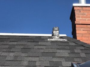 A roof vent pipe and brick chimney on a shingle roof, showing a typical handyman repair area for Elite Roofing Colorado Springs, CO.