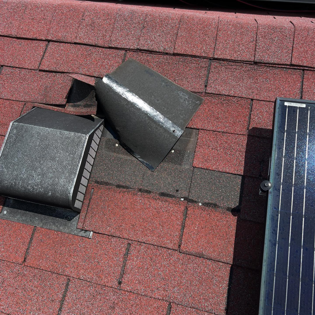Close-up of a red shingle roof with vents and a solar panel, showing a repair area by GOAT Services, LLC in Louisville, KY.