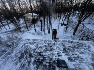 A snowy roof with a chimney and equipment, indicating recent snow or ice removal by BETHO Construction INC in Milford, MA.