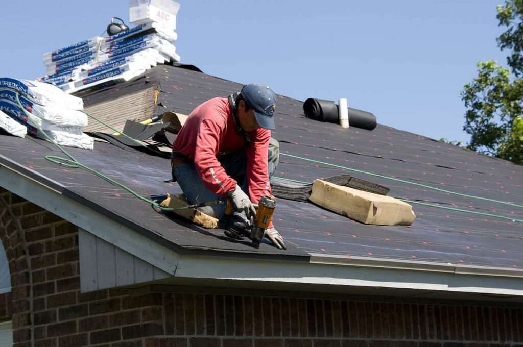 A roofer installing new shingles on a residential roof with a nail gun, demonstrating construction work by AKN Design Group in Fort Worth, TX.