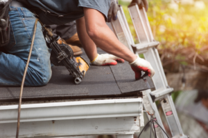 A roofer installing new shingles with a nail gun on a residential roof for Shore Home Construction Roofing in Salisbury, MD.