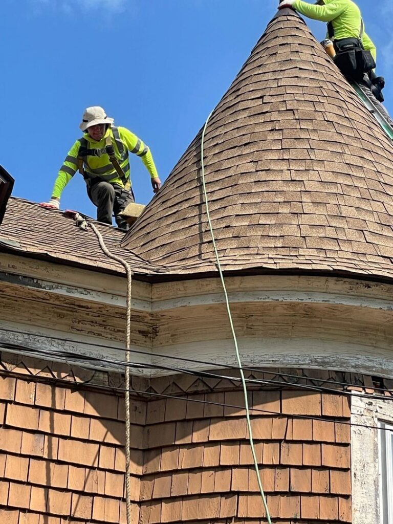 A roofer working on the conical roof of a house, performing repairs by Usa Construction of Danbury LLC in Danbury, CT.