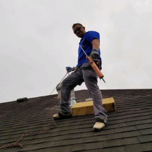 A roofer with a caulk gun and safety gear working on a roof for Rob the Roofer in Houston, TX.