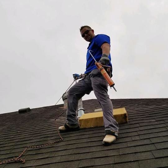 A roofer with a caulk gun and safety gear working on a roof for Rob the Roofer in Houston, TX.