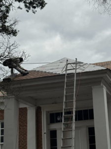 A roofer working on a residential roof with a ladder for Spartan Roofing Systems in Jackson, TN.