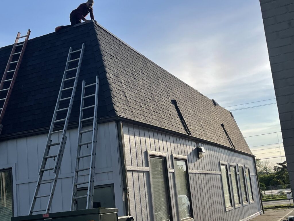 A roofer working on a shingle roof with ladders leaning against the building, by Mp painting and roofing LLC in Dayton, OH