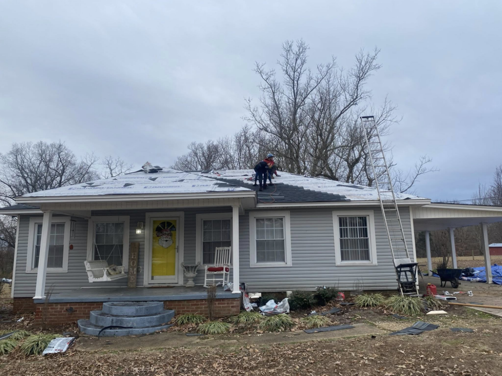 Roofers installing new shingles on a residential house roof with a ladder and materials for Spartan Roofing Systems, Jackson, TN.