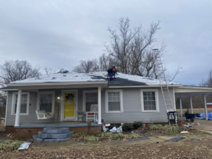 Roofers installing new shingles on a residential house roof with a ladder and materials for Spartan Roofing Systems, Jackson, TN.