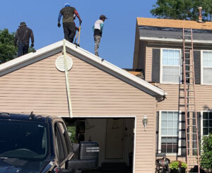 Roofers removing old shingles from a residential roof with a ladder and truck visible by Element Enterprises in Kansas City, MO.
