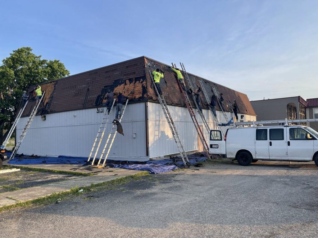 Multiple roofers removing old shingles from a commercial building roof, a service by Mp painting and roofing LLC in Dayton, OH