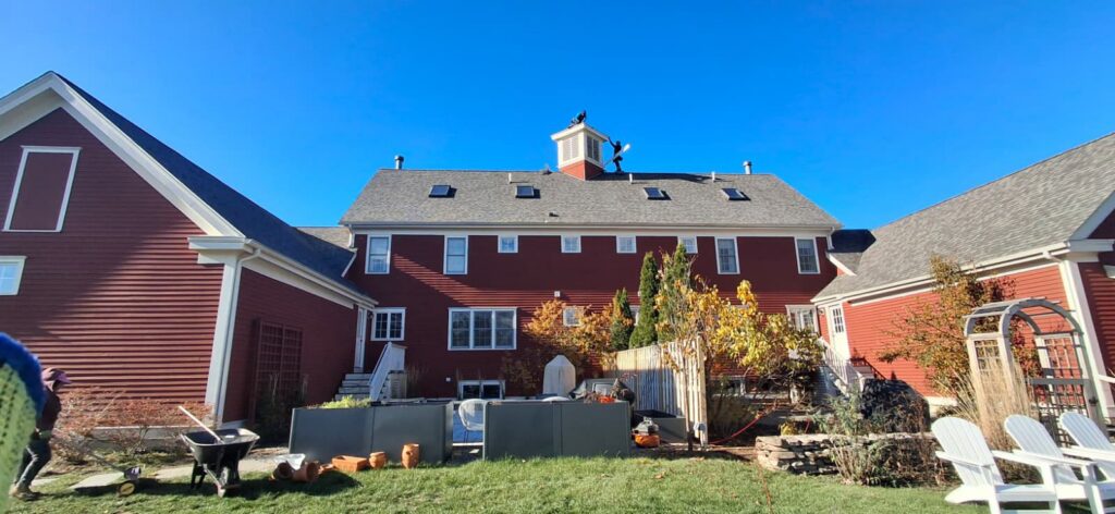 Roofers working on the roof of a large red house, performing a handyman job for Pinguil Roofing Siding Contractor in Lowell, MA.