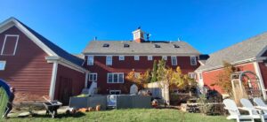 Roofers working on the roof of a large red house, performing a handyman job for Pinguil Roofing Siding Contractor in Lowell, MA.
