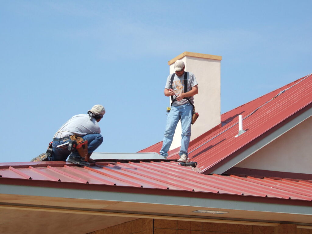 Roofers working on a red metal roof, demonstrating the expertise of Austin Roofing and Construction in Austin, TX.