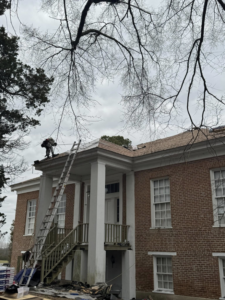 A roofing contractor repairing a house roof with a ladder and materials on the ground for Spartan Roofing Systems, Jackson, TN.