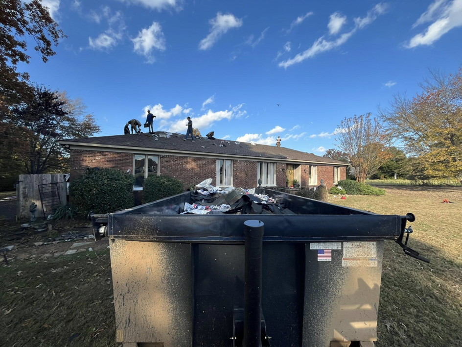 Roofing crew working on a house roof with a large dumpster for debris removal by Skyline Roofing L.L.C in Jackson, TN.
