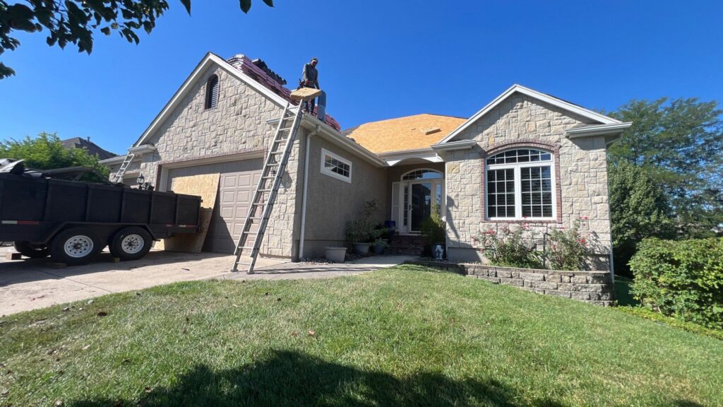 A roofing crew installing new shingles on a house with a dump trailer in the driveway by Element Enterprises in Kansas City, MO.