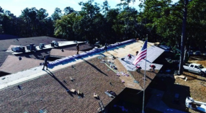 An aerial view of a roofing crew actively installing new shingles on a large roof by Charleston Roofs & Windows in North Charleston, SC.