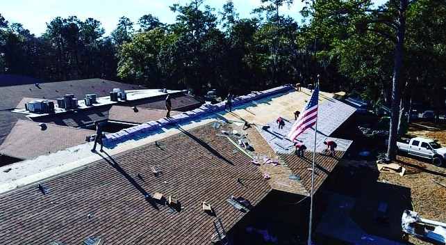 An aerial view of a roofing crew actively installing new shingles on a large roof by Charleston Roofs & Windows in North Charleston, SC.