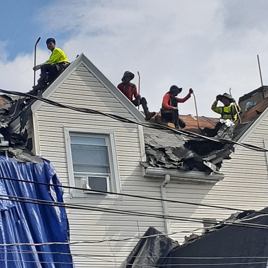 A roofing crew from Manny's Sb Construction Inc removing old shingles from a residential roof in Goshen, NY.