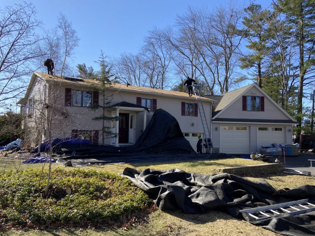 A roofing crew performing a roof replacement with protective tarps on the ground by Eagle Exteriors in Cumberland, RI.