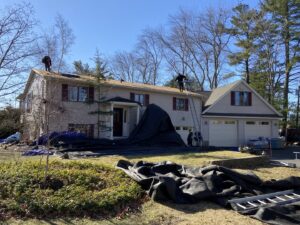A roofing crew performing a roof replacement with protective tarps on the ground by Eagle Exteriors in Cumberland, RI.