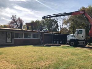 A roofing crew using a crane to lift materials during a roof installation by Gwen Co in St. Louis, MO.